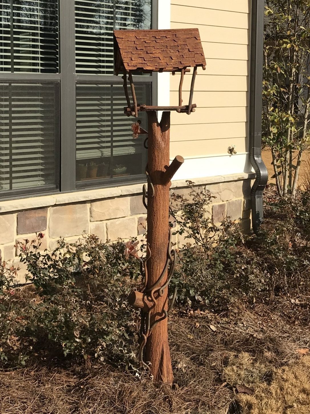 A wooden bird feeder is sitting in front of a house.