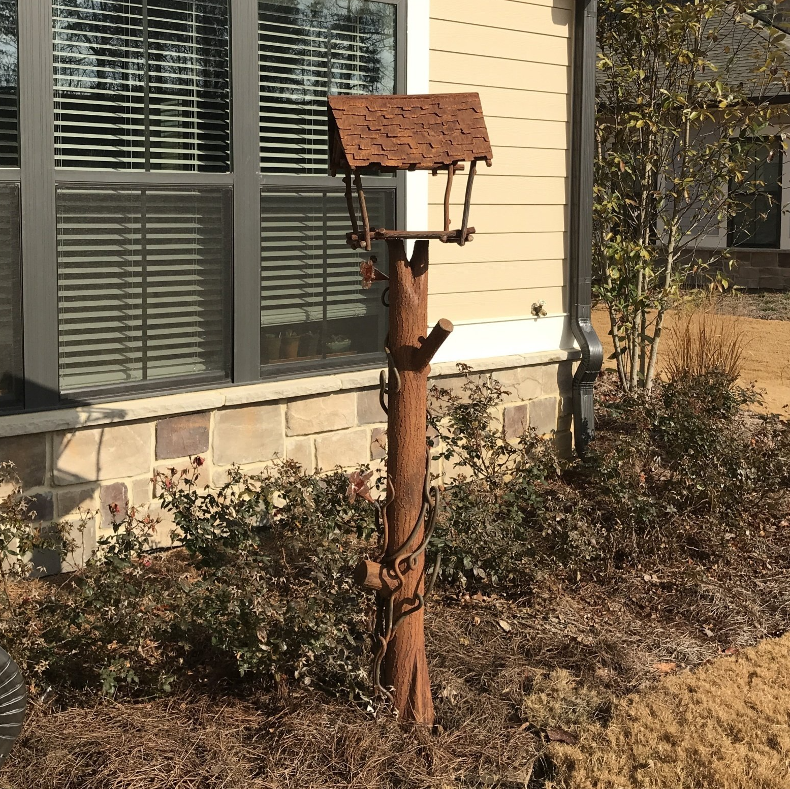A rusty bird feeder is sitting in front of a house
