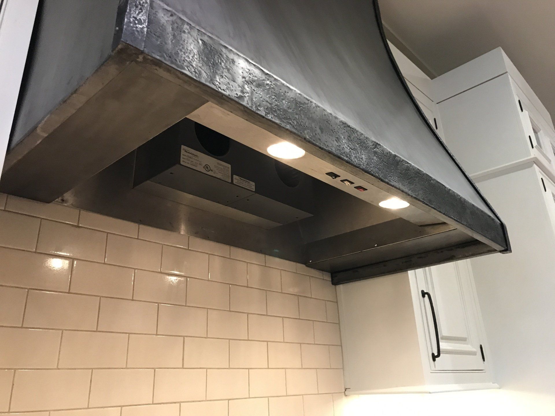 A kitchen with white cabinets and a black hood above the stove.