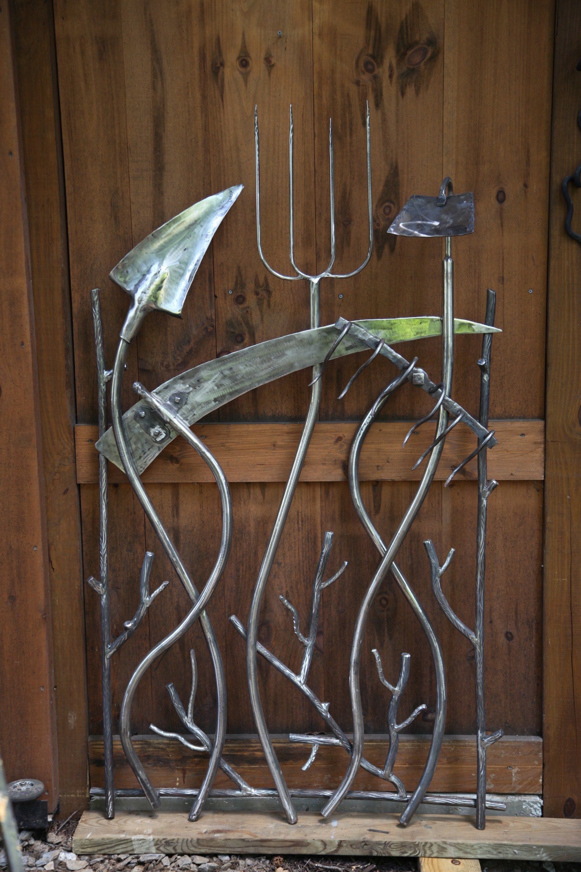 A wrought iron gate with a shovel , rake , and fork on it.