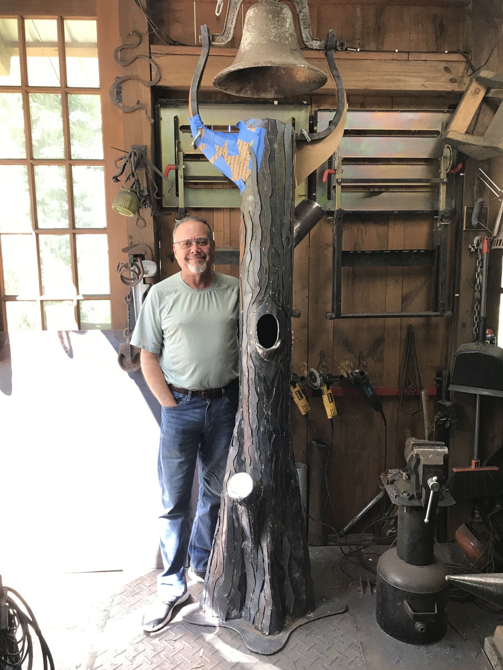 A man standing next to a tree trunk with a bell on top of it