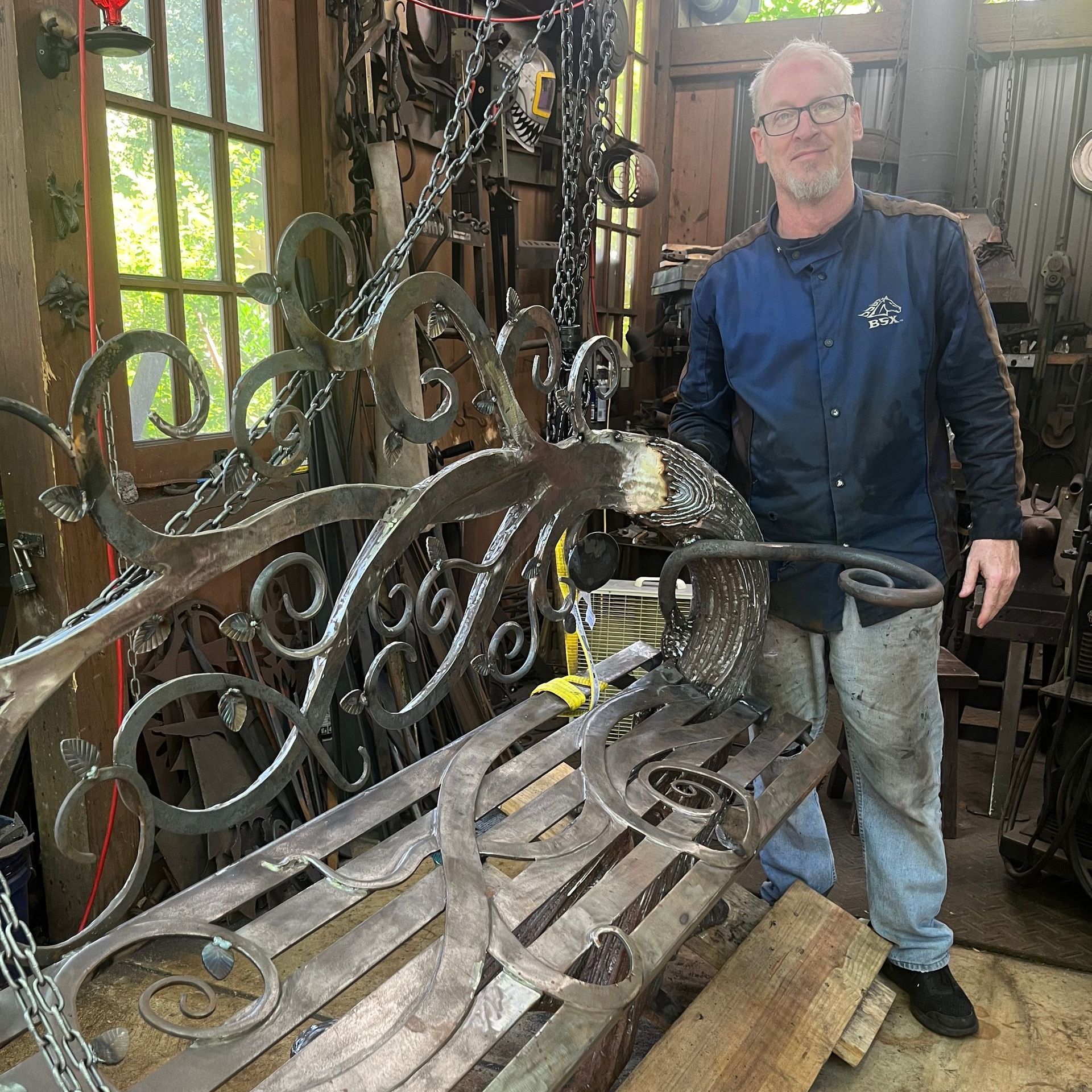 A man is standing next to a wrought iron bench in a workshop.