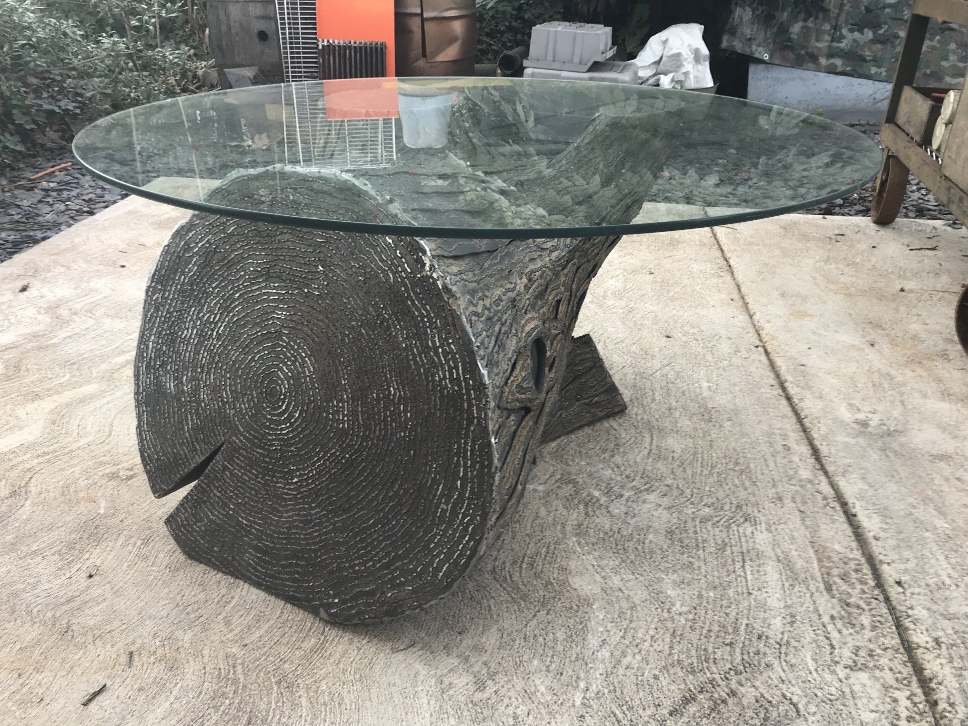 A glass table with a wooden base is sitting on a sidewalk.