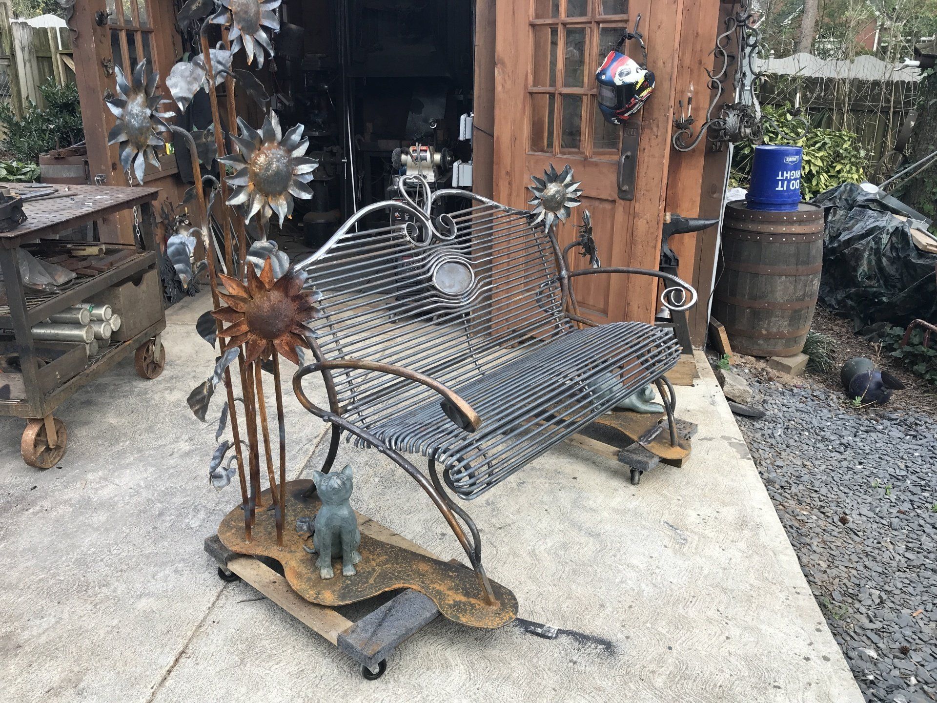 A wrought iron bench is sitting on the sidewalk in front of a wooden building.
