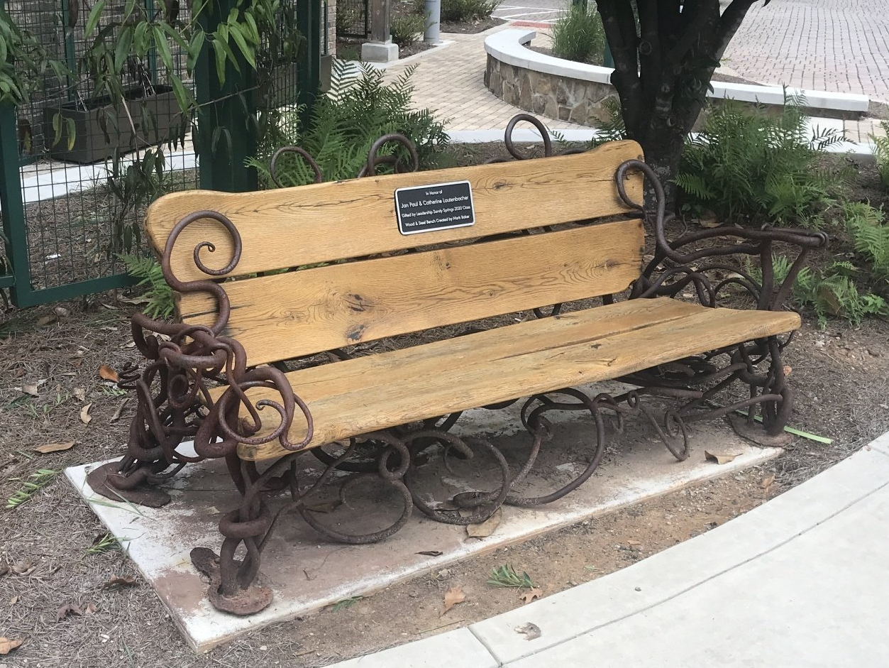 A wooden bench with a metal frame is sitting on a sidewalk.