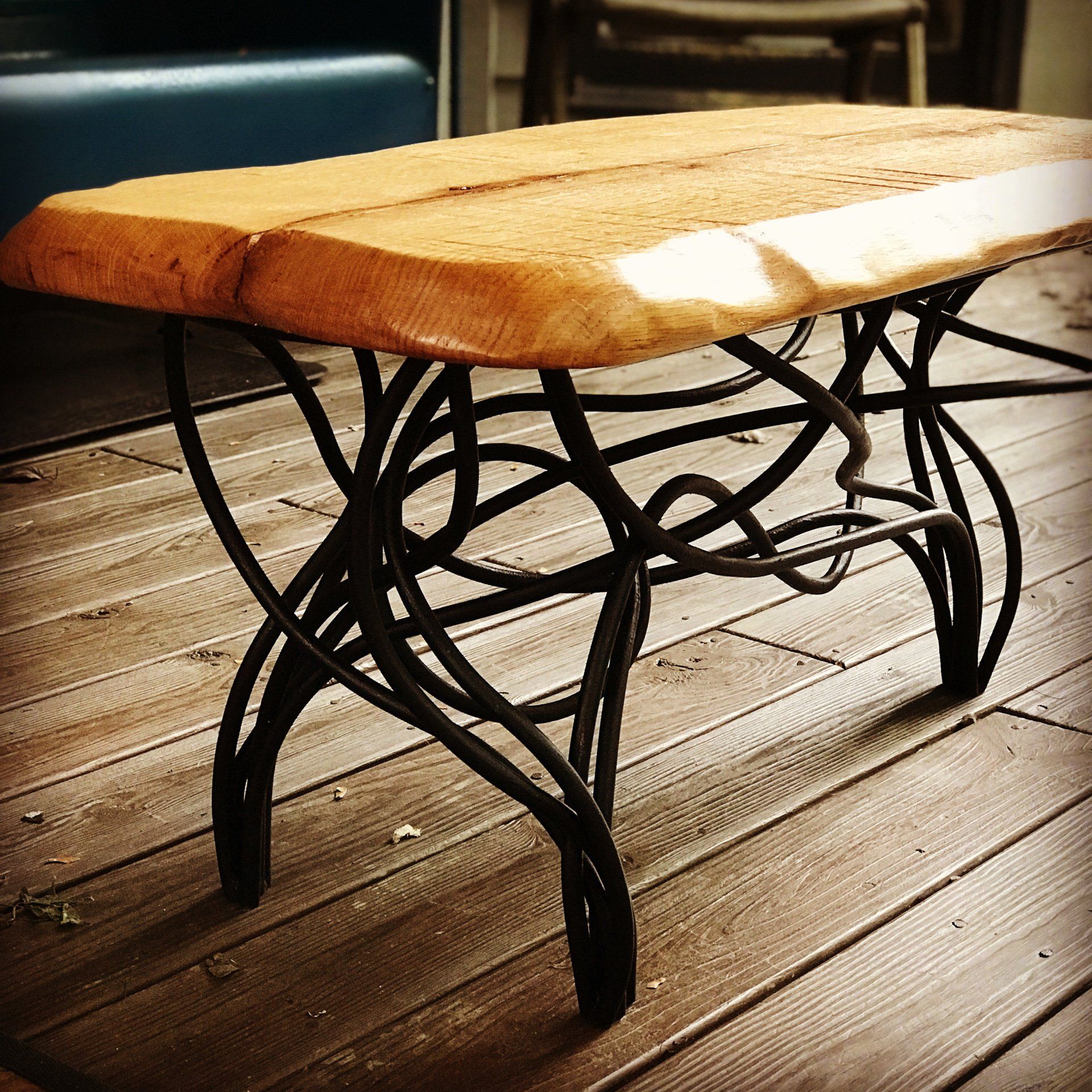 A wooden table with a wrought iron base sits on a wooden deck