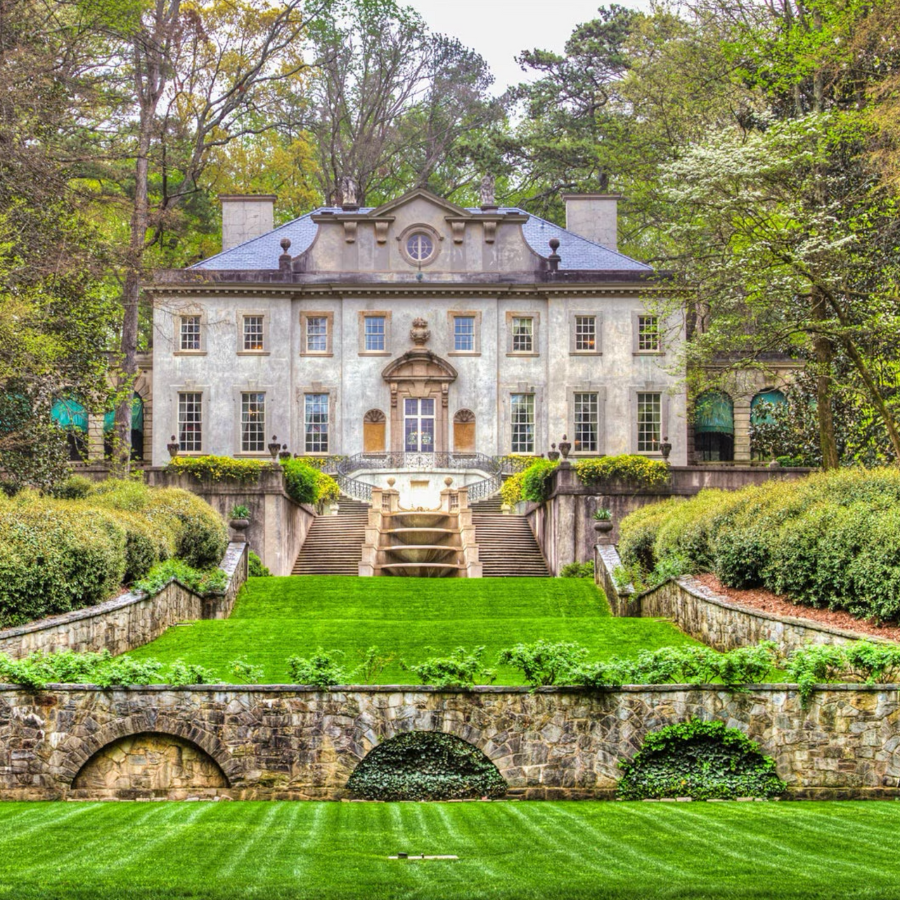 A large white house is surrounded by trees and a lush green lawn.
