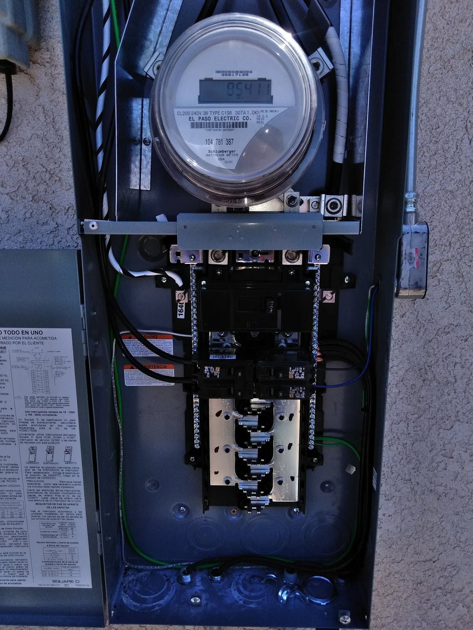 Electric meter and breaker panel mounted on a wall, with exposed wiring and open cover.