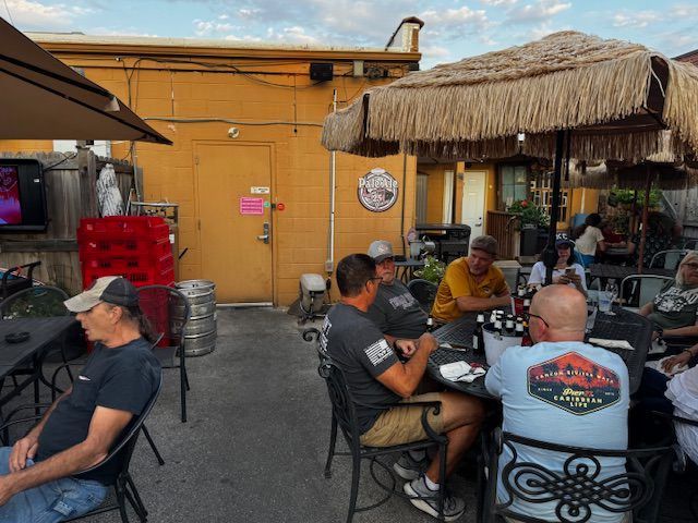 Outdoor patio with people seated at tables, under umbrellas, near a yellow building.