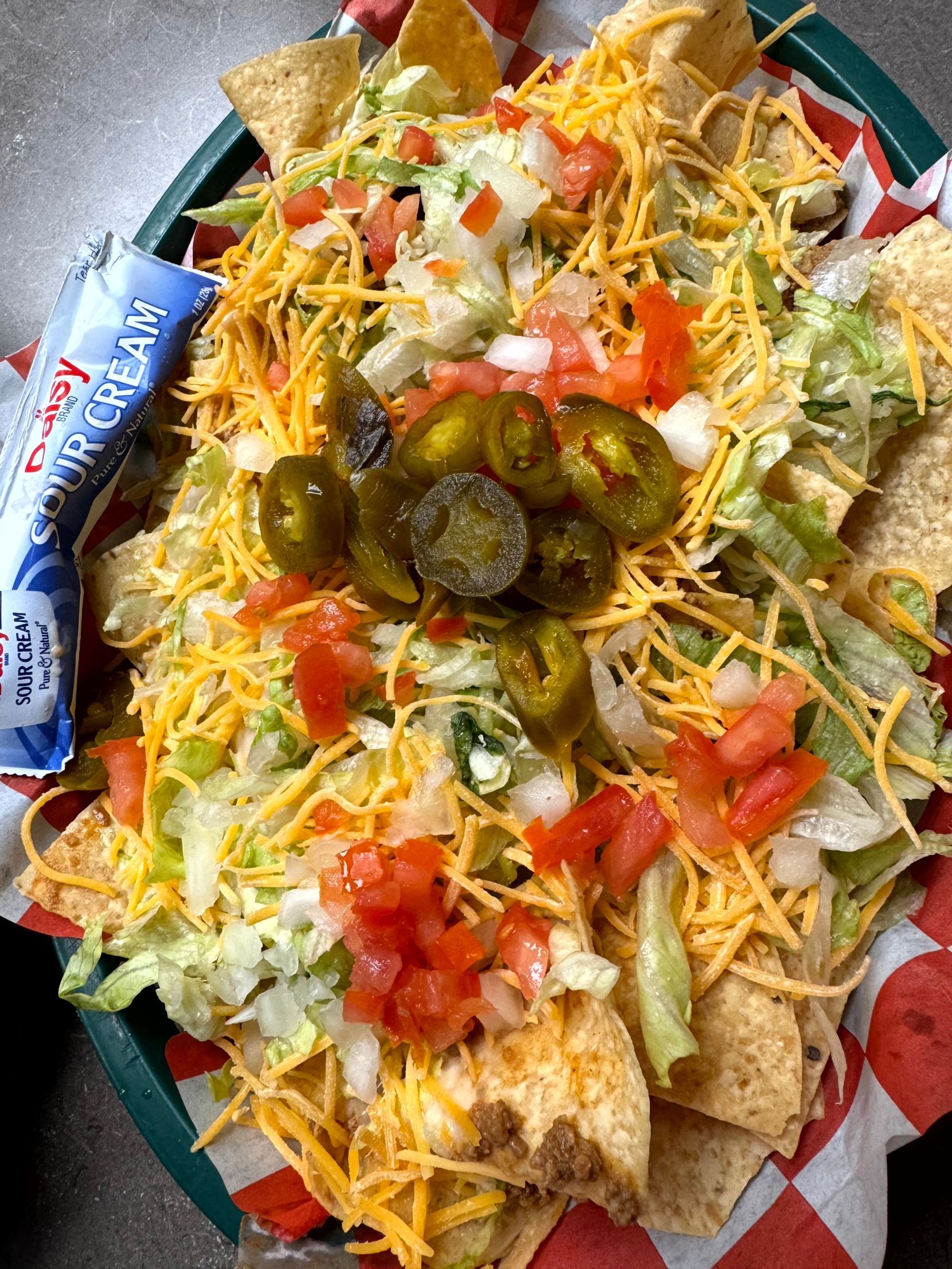 Nachos with shredded cheese, tomatoes, onions, jalapeños, and lettuce, served in a basket.