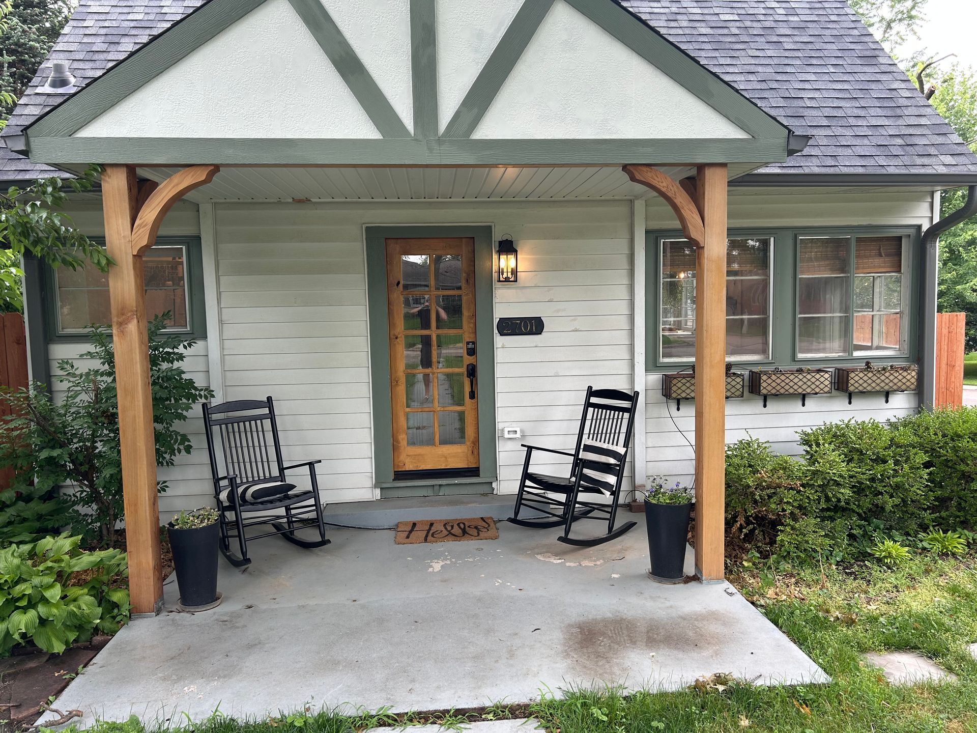 A small white house with a porch, rocking chairs, and a brown door.