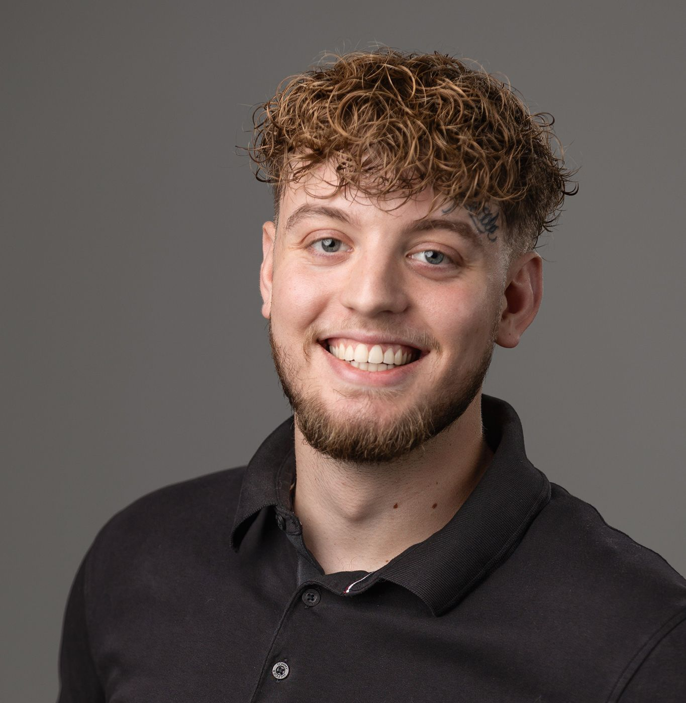 Smiling young man with curly brown hair and beard, wearing a black shirt.