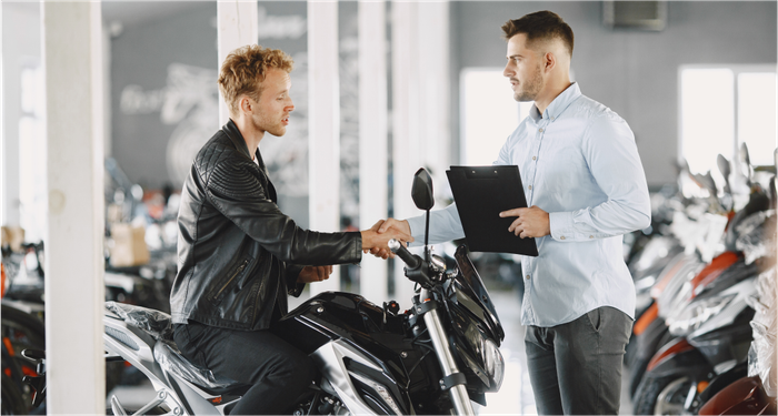um homem está sentado em uma motocicleta apertando a mão de um homem em um showroom de motocicletas.