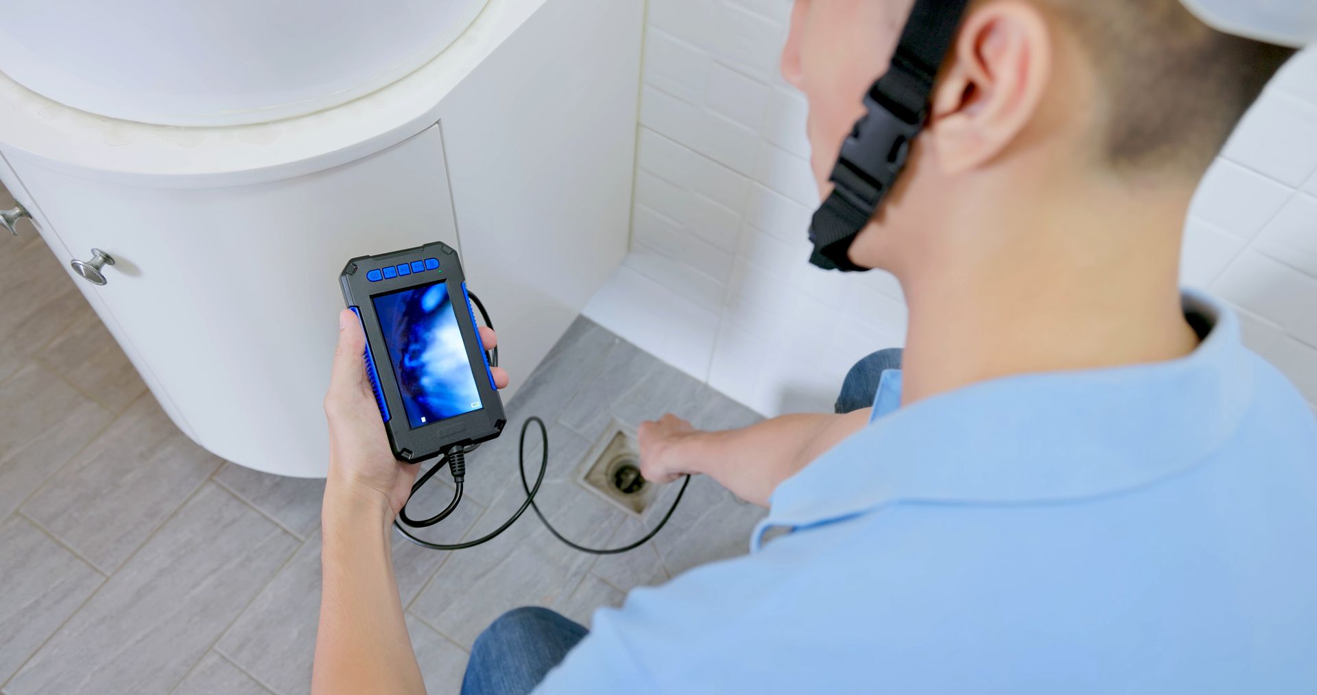 An Asian technician using an inspection camera to check the bathroom drain near the cabinet