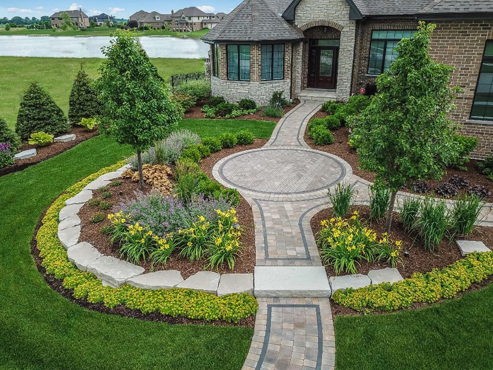 An aerial view of a house with a circular walkway surrounded by flowers and trees.