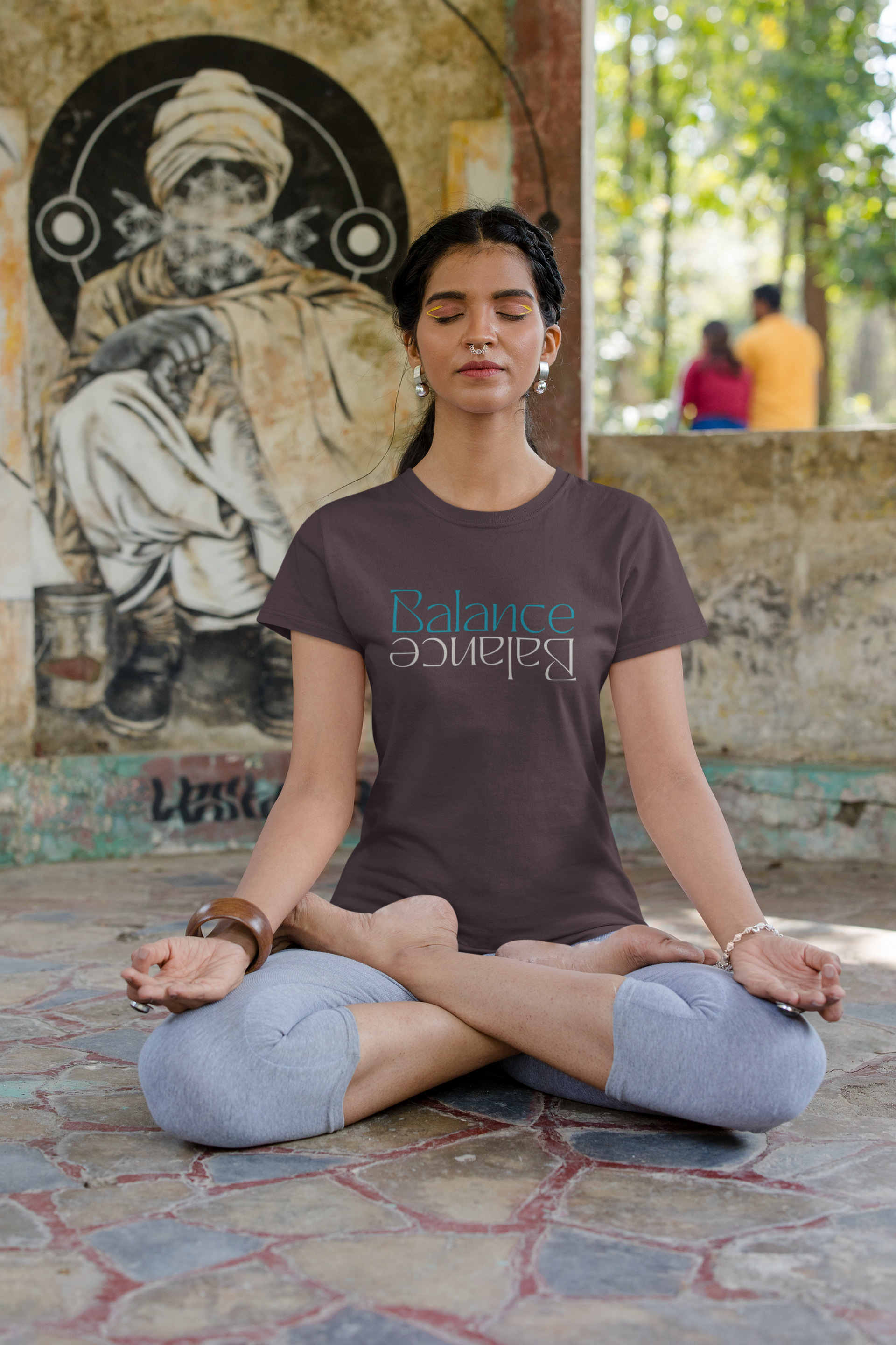 A woman is sitting in a lotus position on the ground with her eyes closed.