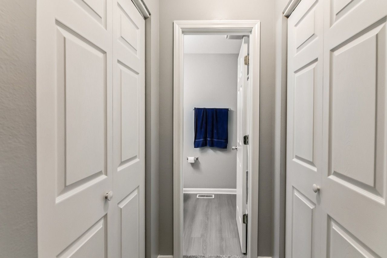 Narrow hallway with white doors on both sides, leading to a bathroom with blue towels.