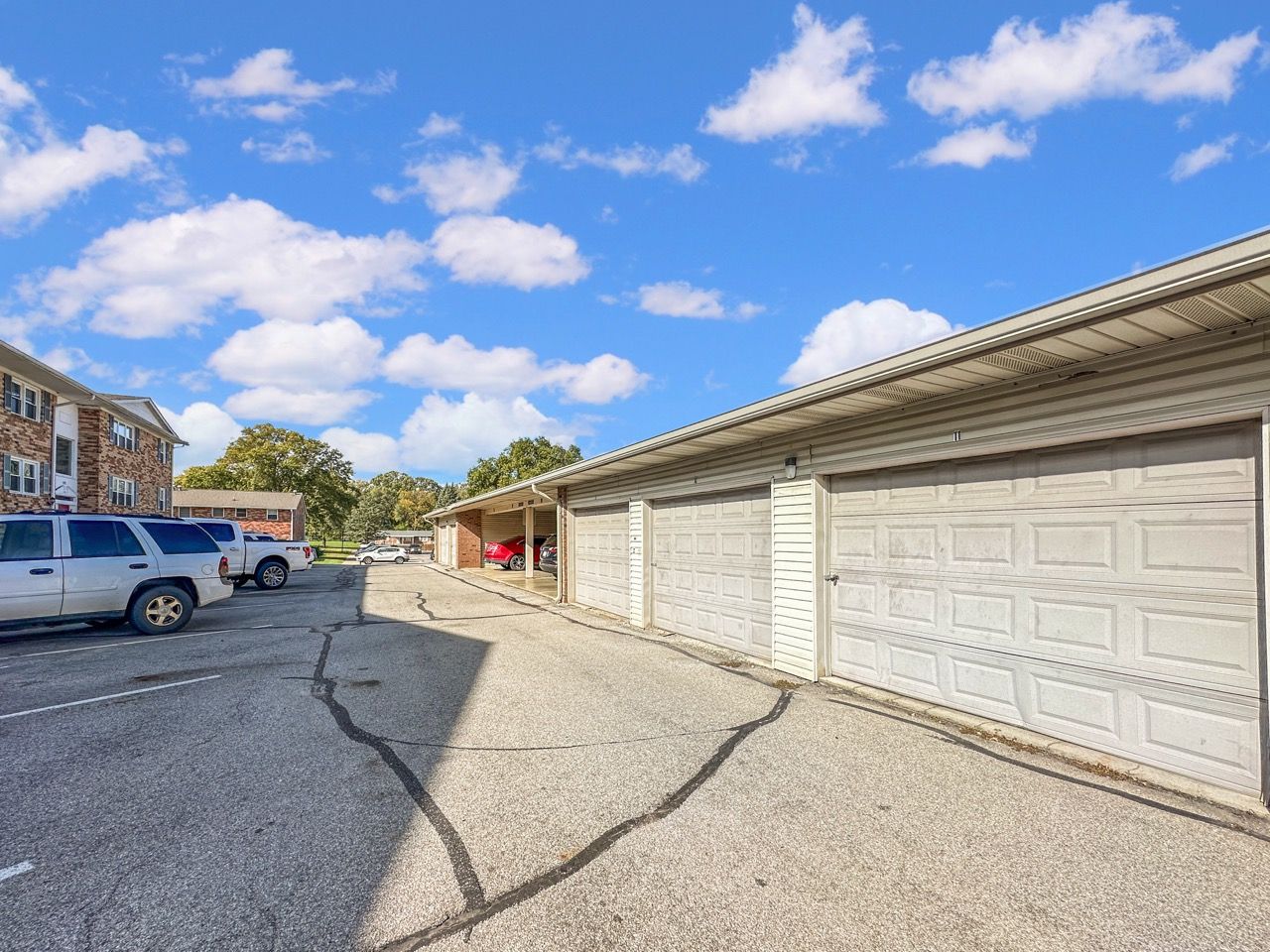 Parking area with a row of attached garages under a cloudy blue sky.