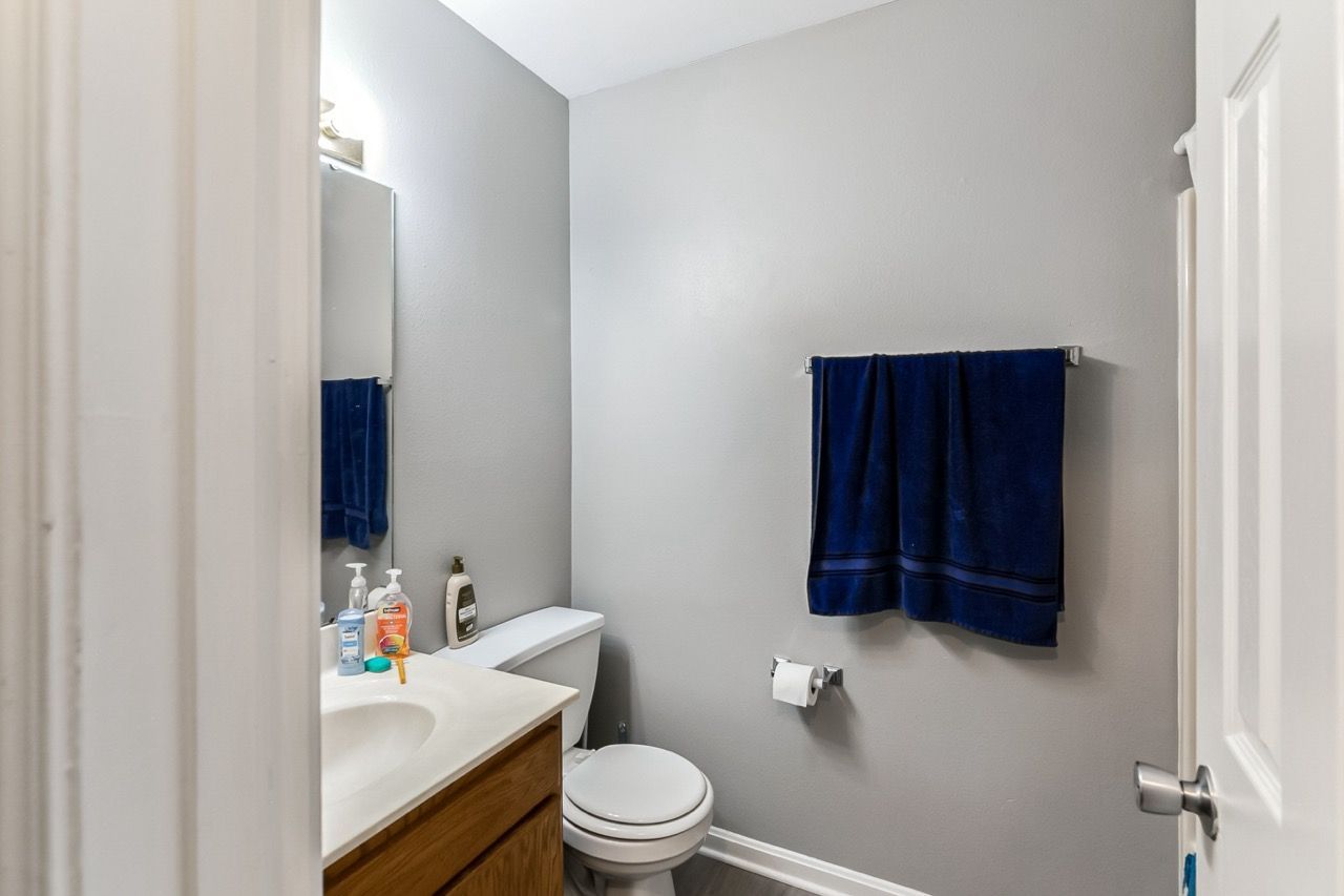 Bathroom with gray walls, white trim, and a blue towel rack. A toilet, sink, and mirror are visible.