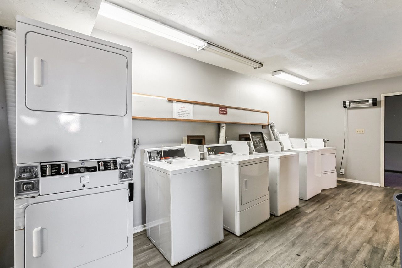Laundry room with white washers and dryers, a shelf, and fluorescent lighting.