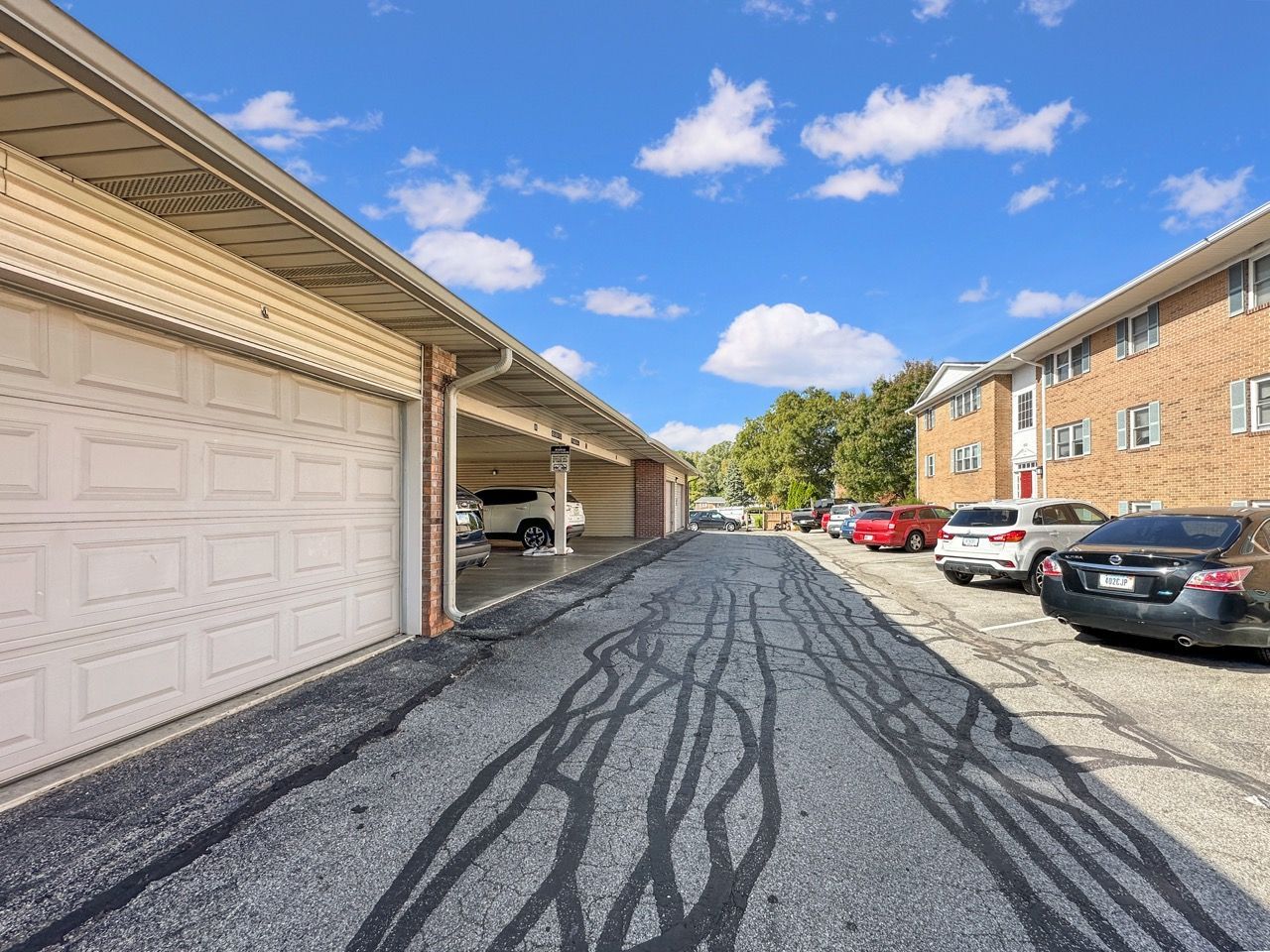Asphalt driveway between garages and apartment building, parked cars.