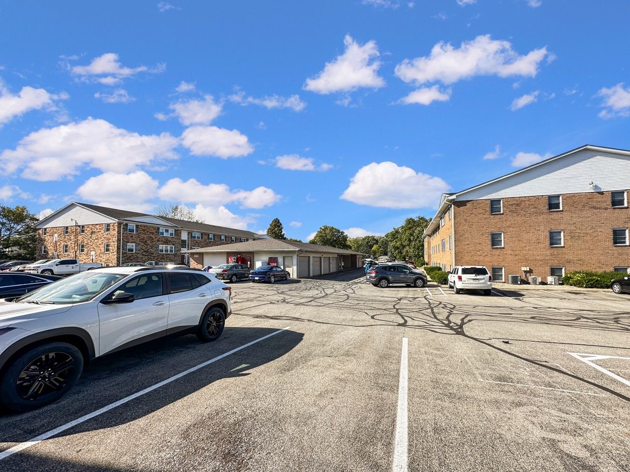 Parking lot with cars, brick apartment buildings, and a blue sky with clouds.
