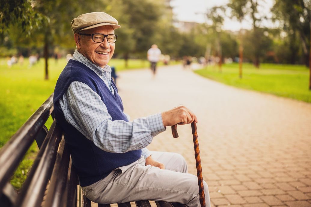 An elderly man is sitting on a park bench with a cane.
