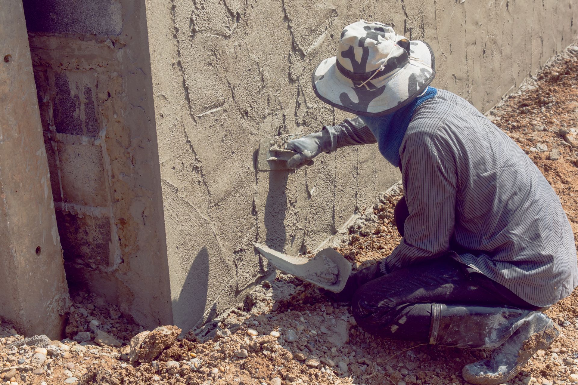 Woman in a hard hat and overalls with a putty knife giving a thumbs-up in front of a drywall patch.
