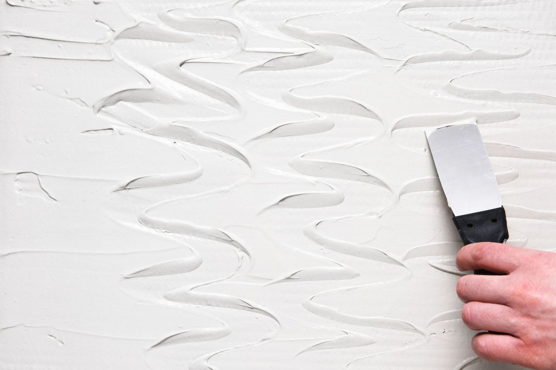 A person is holding a spatula over a white wall.