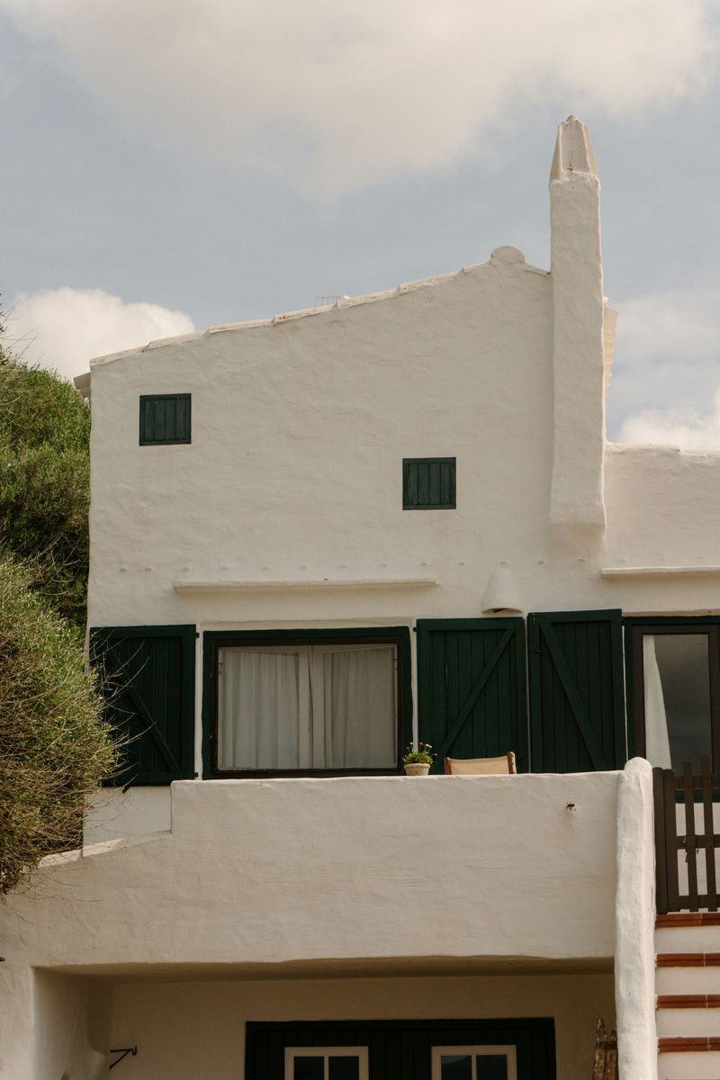 A white house with green shutters on the windows and a balcony.