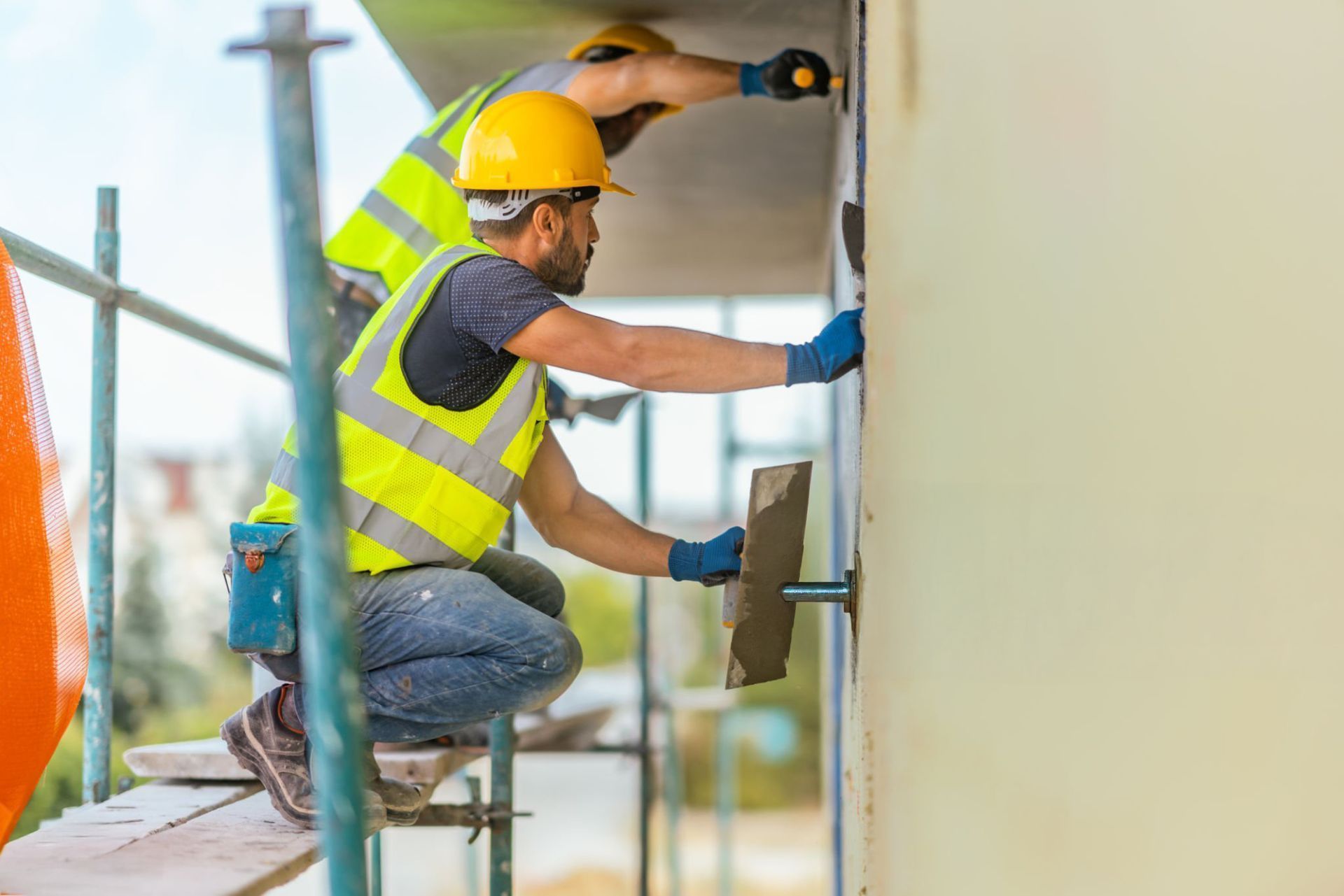 Two construction workers are working on a building on scaffolding. Two construction workers are working on a building on scaffolding.