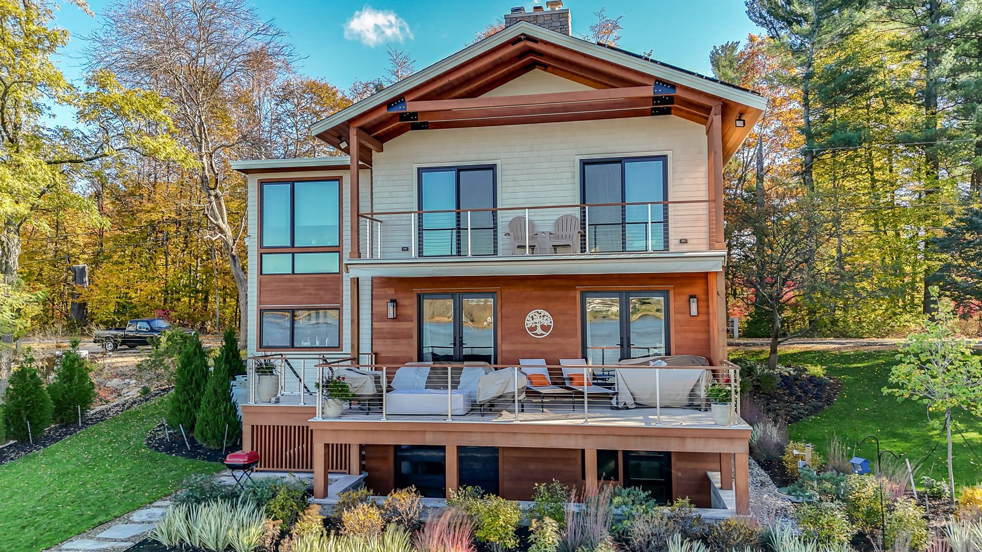 Two-story house with decks, lake view, and autumn foliage.