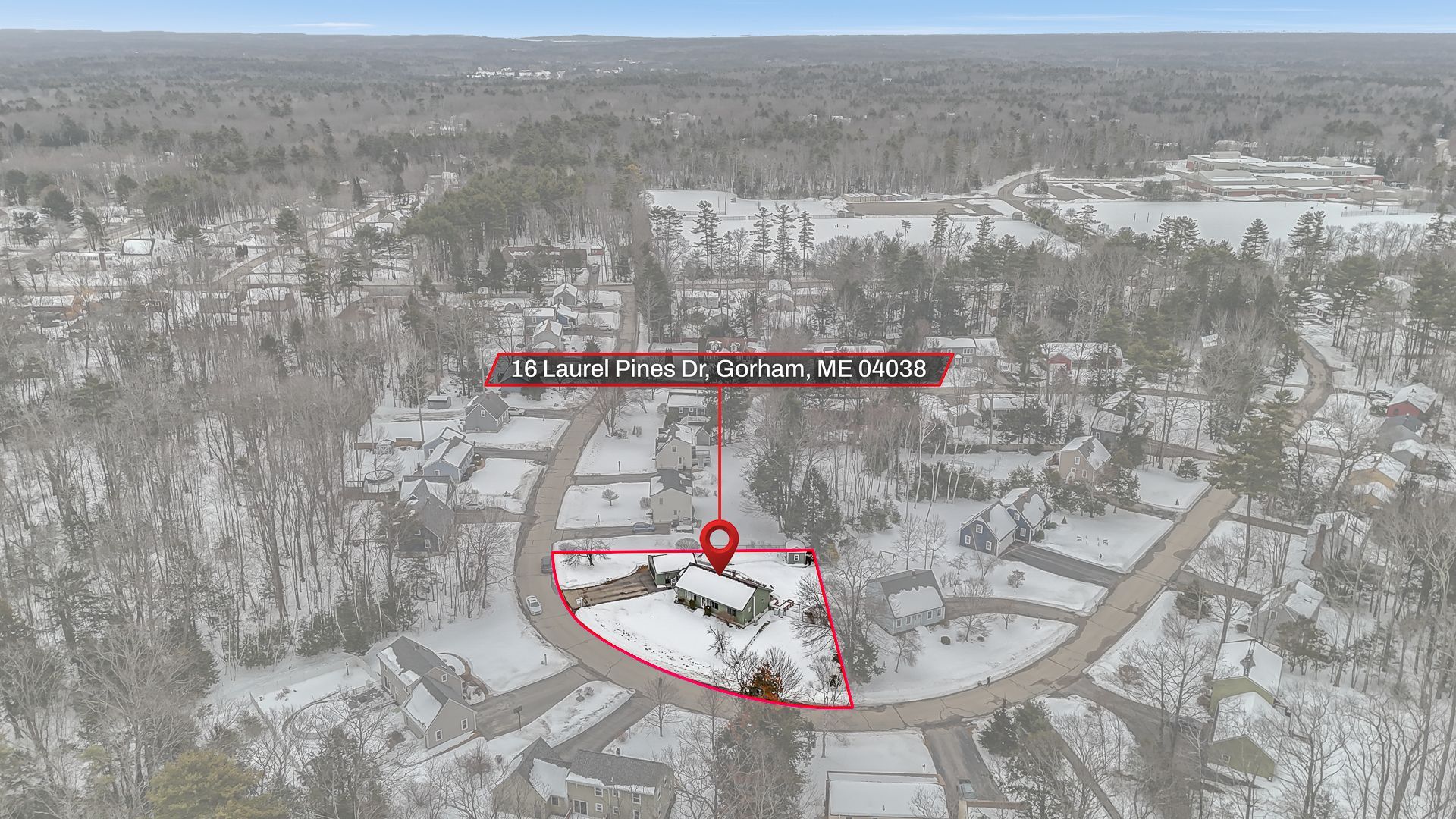 Aerial view of a modern house with a pool and dark roof, surrounded by lush green trees.