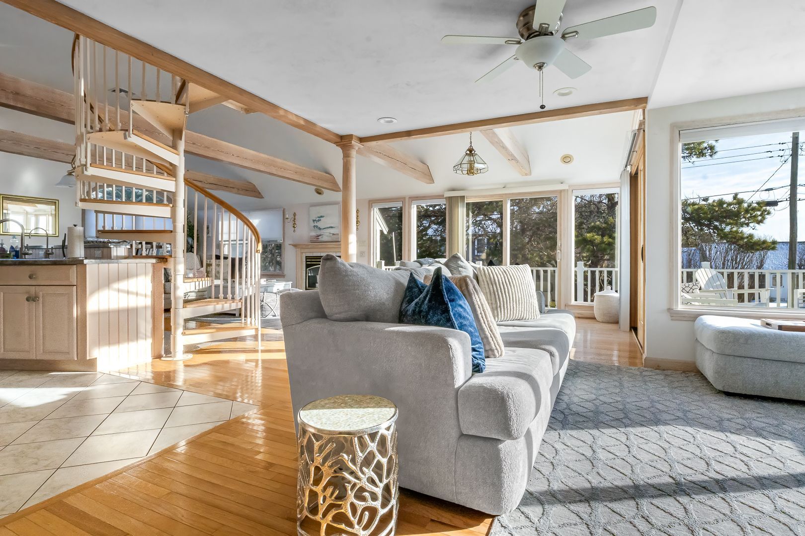 Bright living room with gray couch, spiral staircase, and large windows.