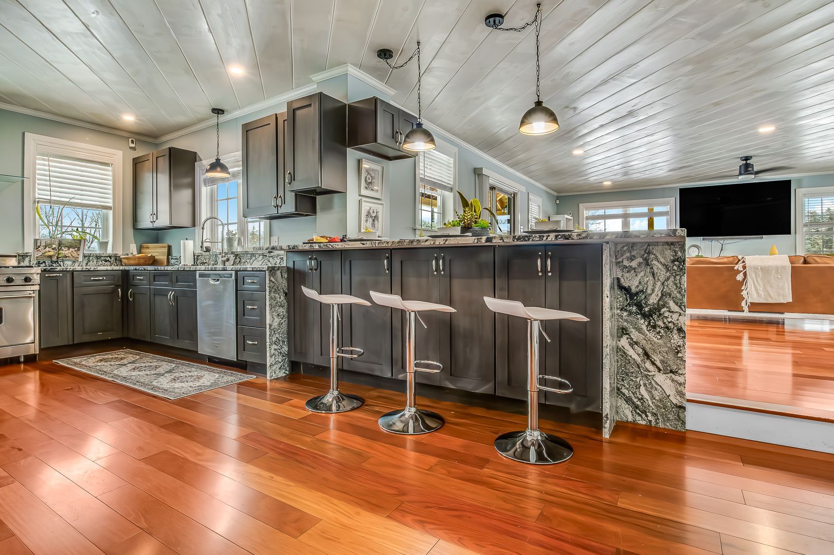 Kitchen with dark cabinets, granite counters, bar stools, wood floor, and white ceiling.
