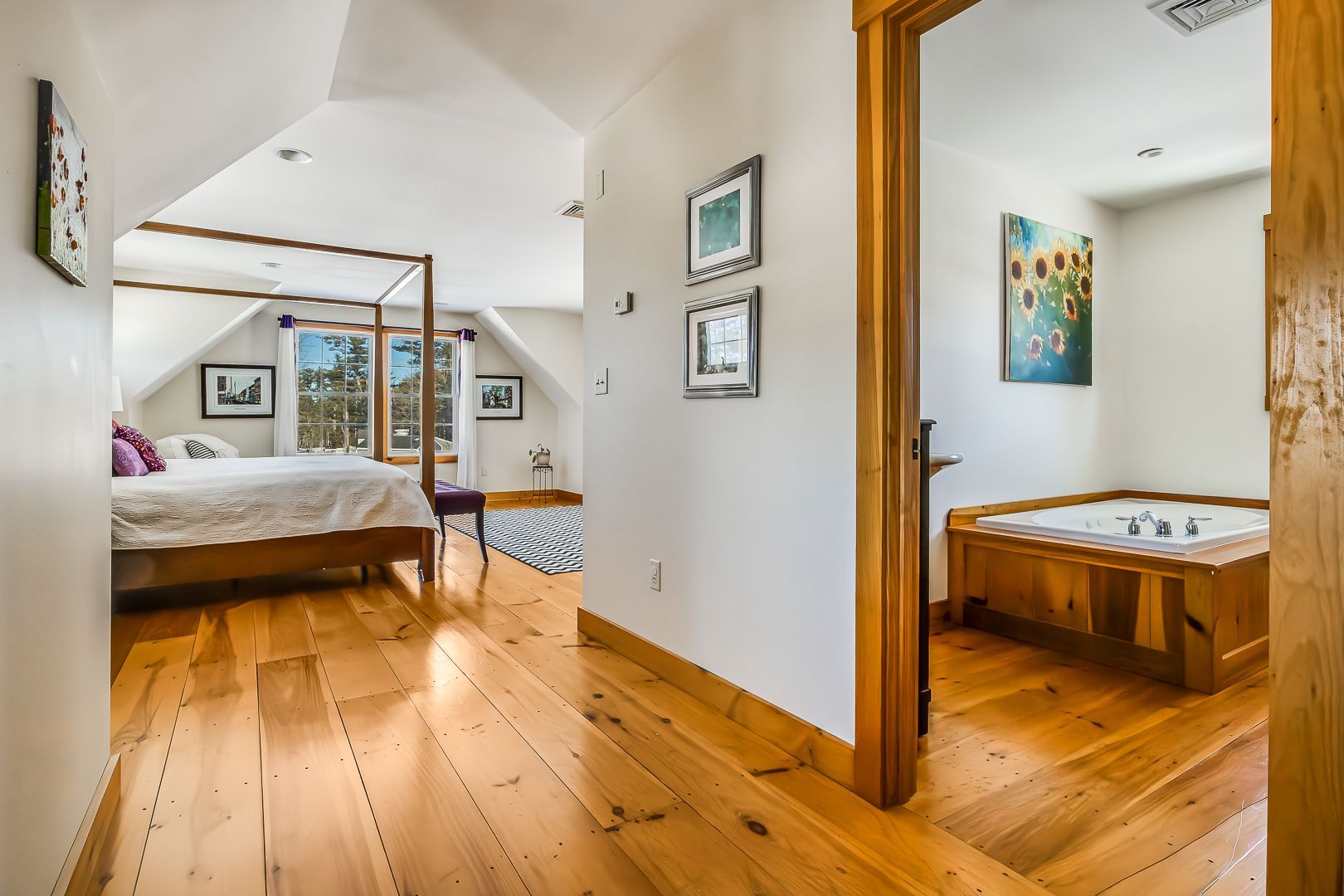 Hallway leading to bedroom with four-poster bed, and bathroom with wooden bathtub. Bright, natural light.