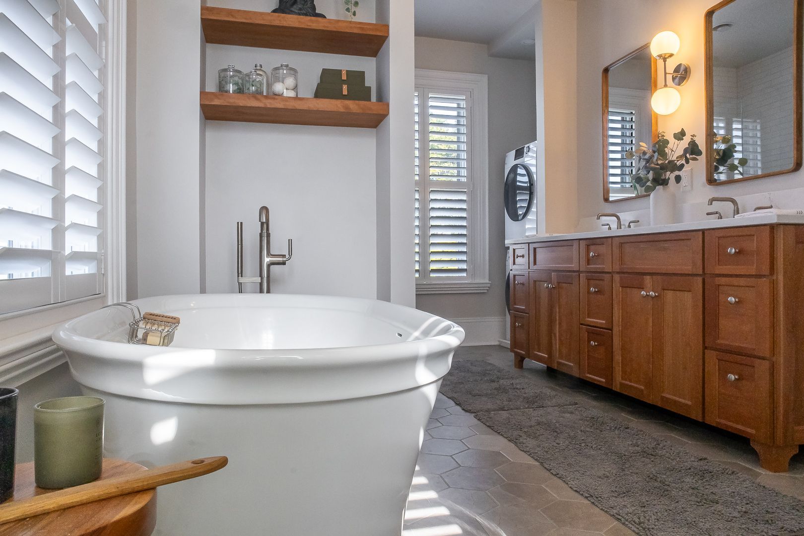 Bathroom with a white soaking tub, wooden vanity, and white shutters.