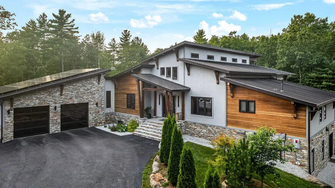 Modern home exterior with stone and wood accents; driveway and trees.