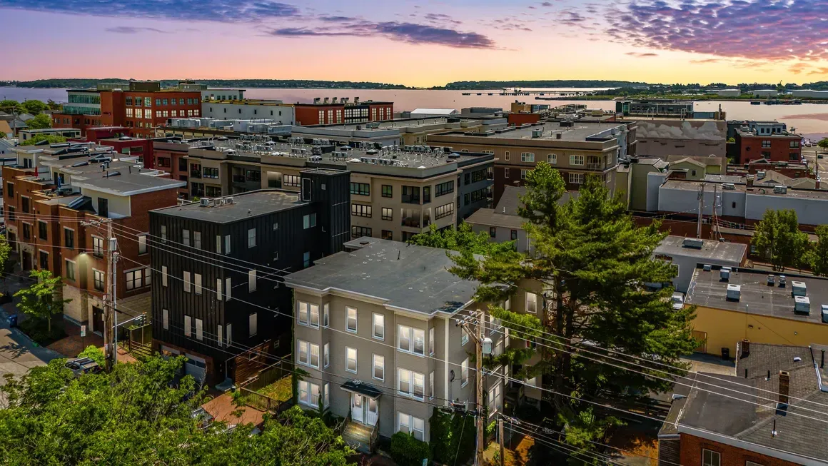 Aerial view of city buildings with a body of water in the background at sunset.