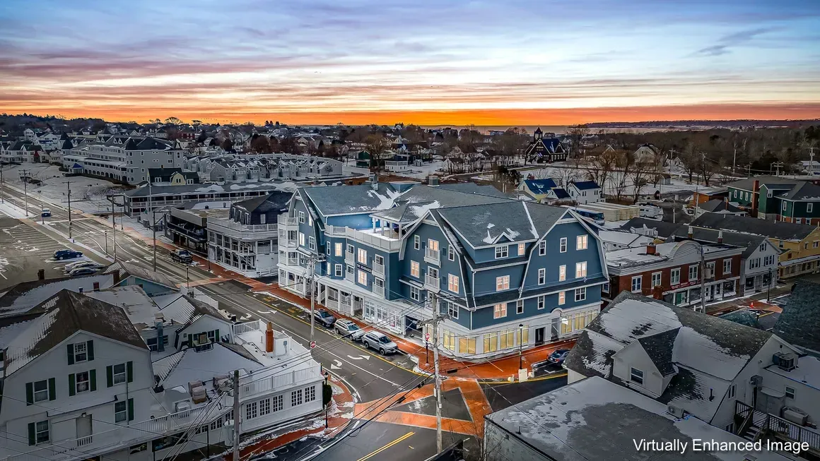 Aerial view of a snowy town at dawn with a blue-roofed hotel on a corner, buildings, and a colorful sky.