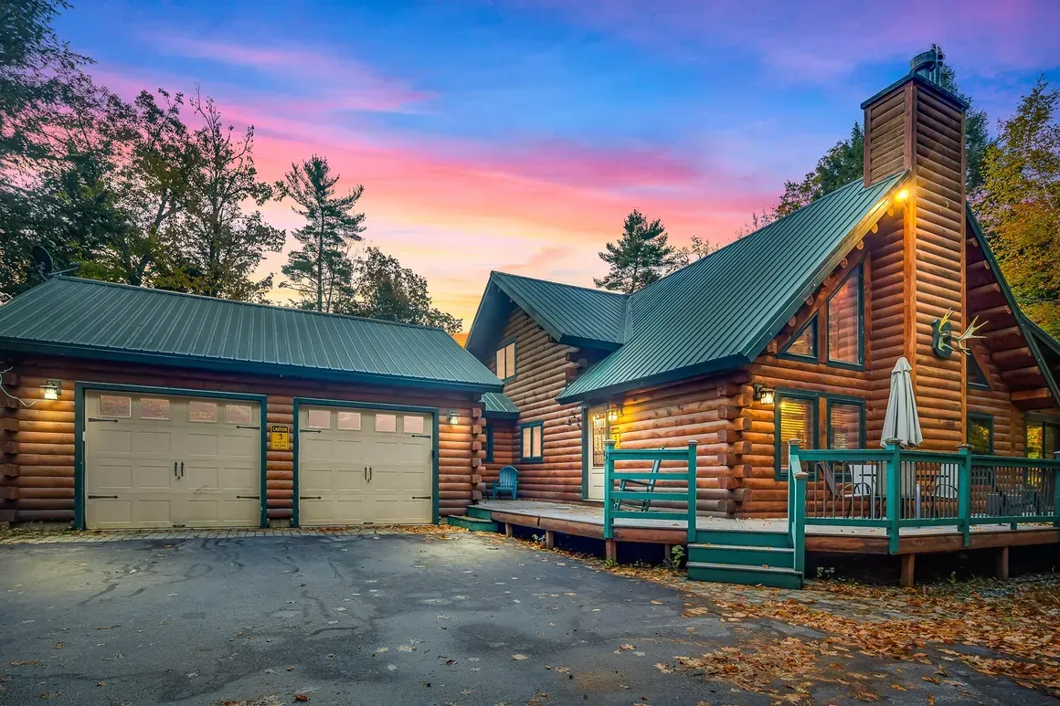 Log cabin home with attached garage under a colorful sunset.