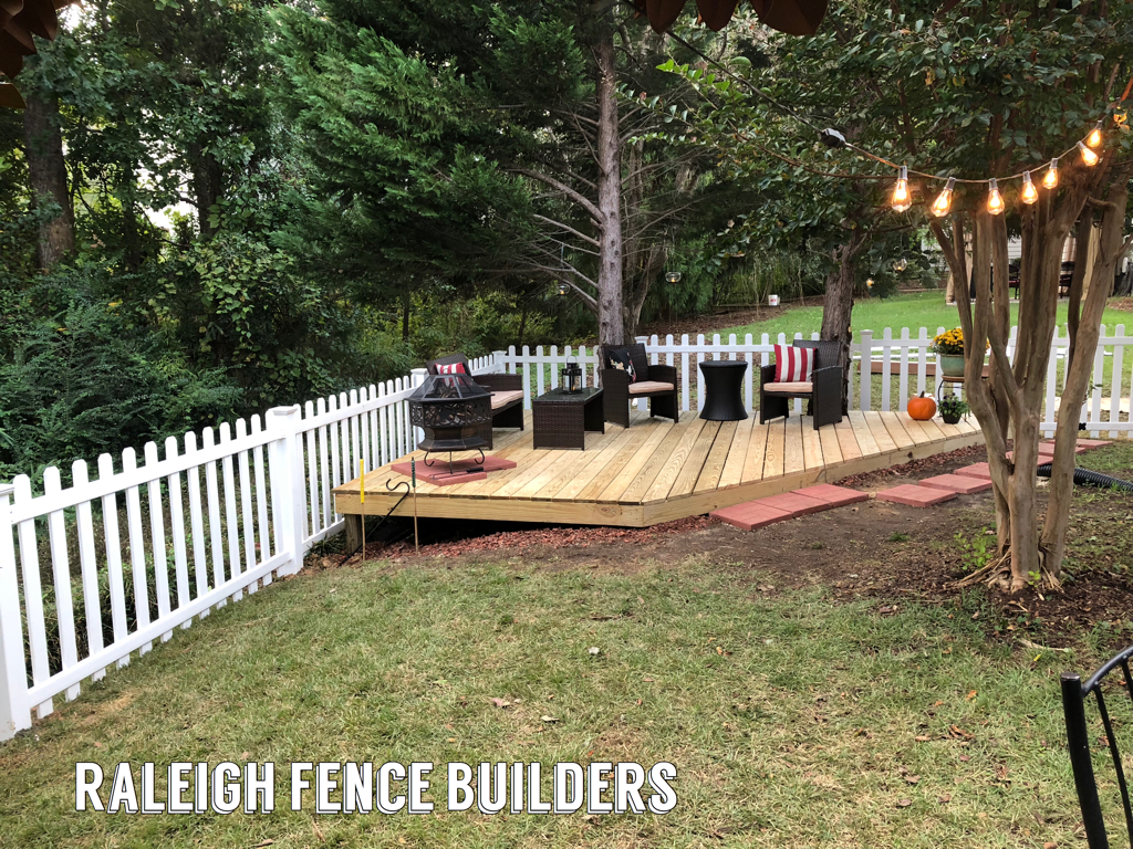A backyard with a wooden deck and a white picket fence.