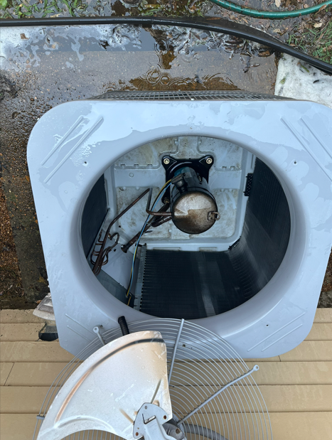 Air conditioning unit, top view with fan blades detached, motor visible. Outdoors, wet surface.