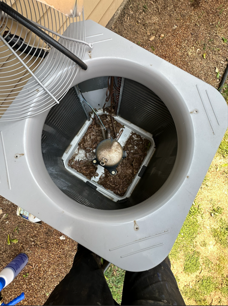 Overhead view of an air conditioning unit with a fan and debris inside the central cage.