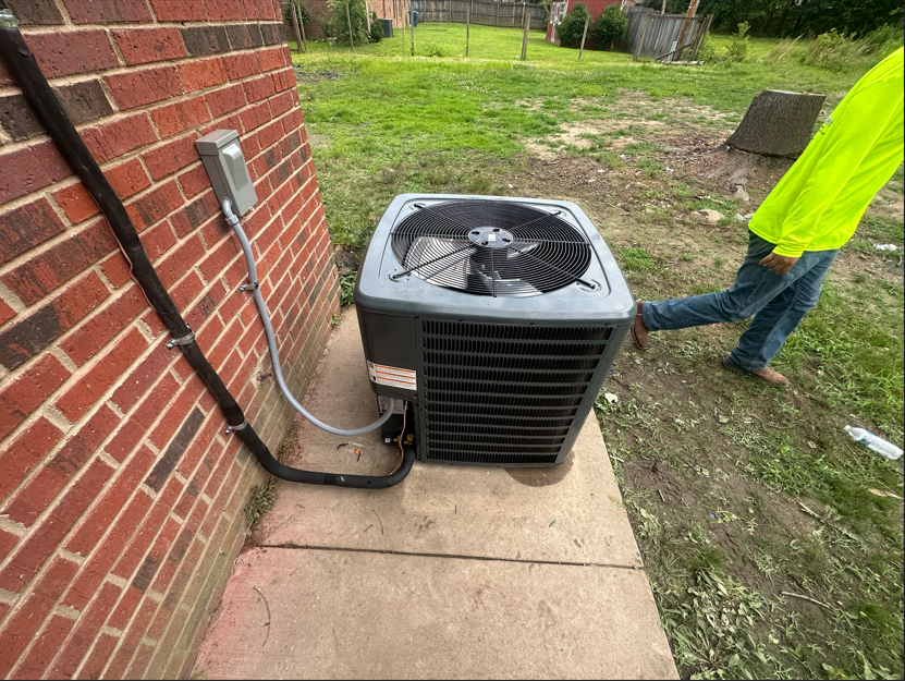 HVAC unit beside a brick wall. A person in yellow leans near it outside.