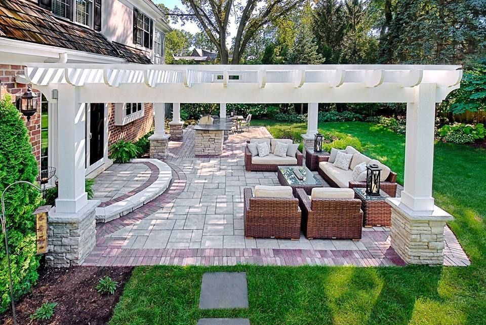 A patio with a pergola and wicker furniture in front of a house