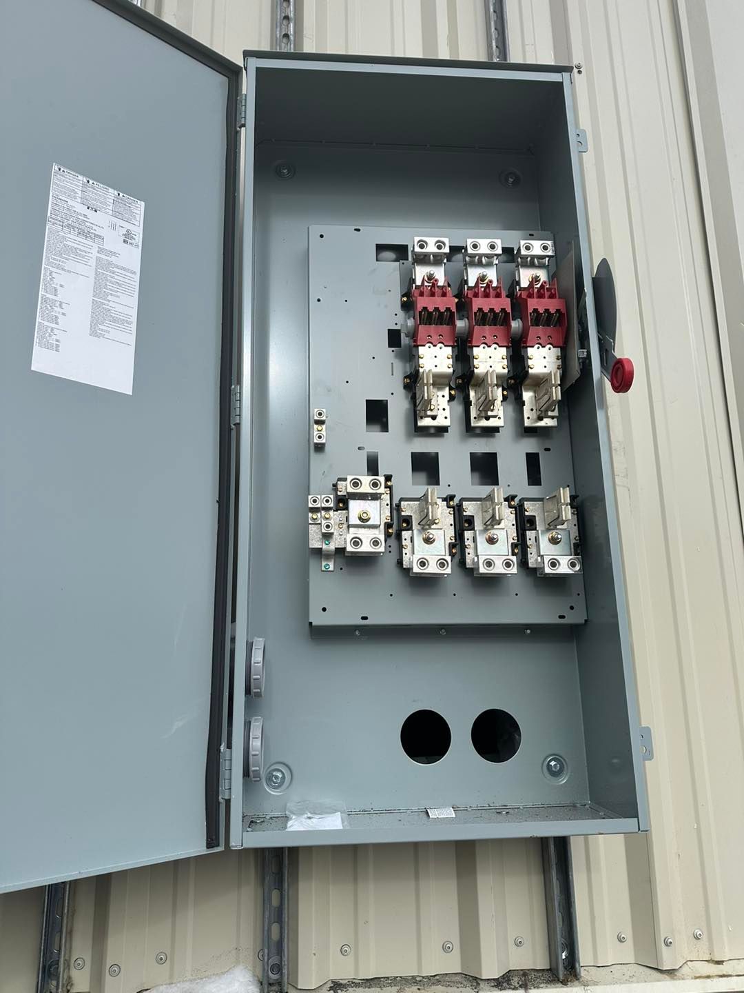 Open electrical panel with switches and fuses. Gray metal box mounted on a wall.