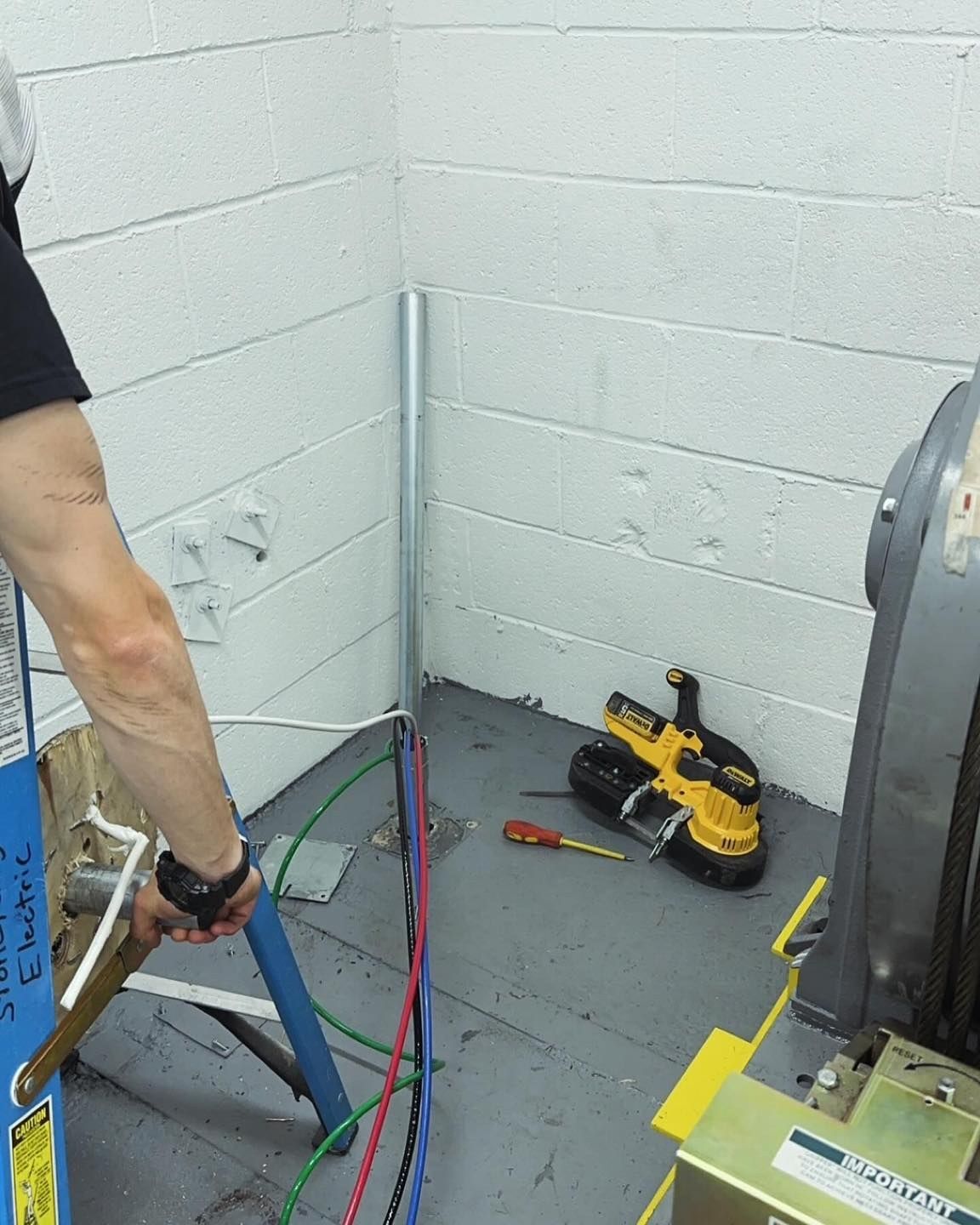 Person working on electrical wiring in an industrial setting, with tools and conduit.