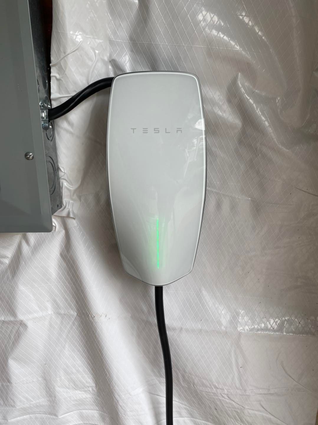 Tesla EV charger with a green light on a white wall.