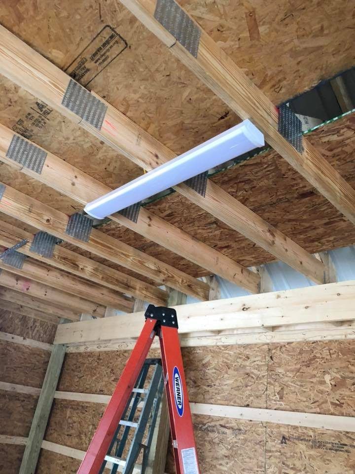Red ladder beneath a white, rectangular ceiling light fixture in a wooden-framed structure with exposed beams.